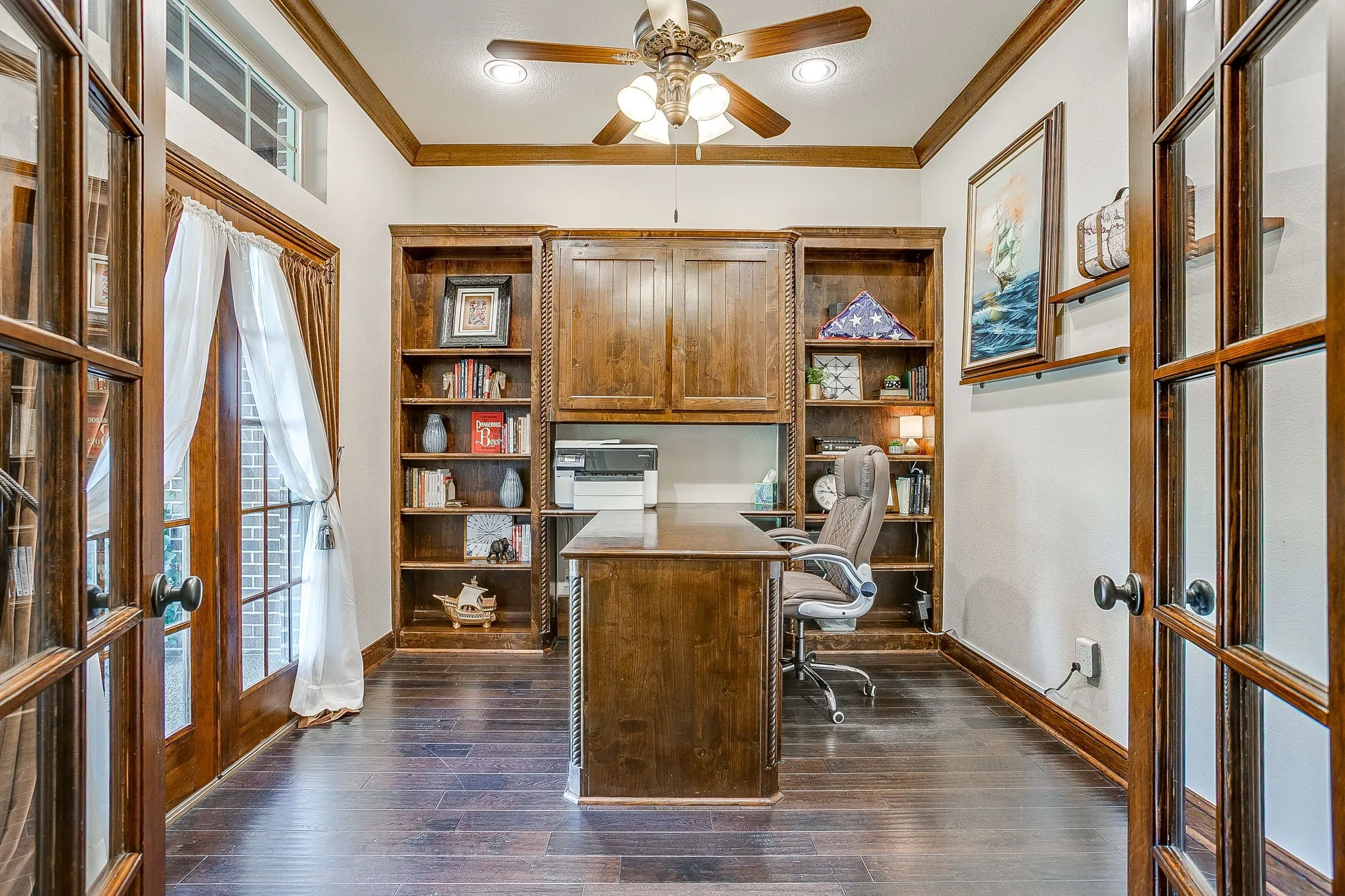 French doors with transom window, wood-finish flooring, built-in cabinetry, ceiling fan with integrated lighting, and crown molding