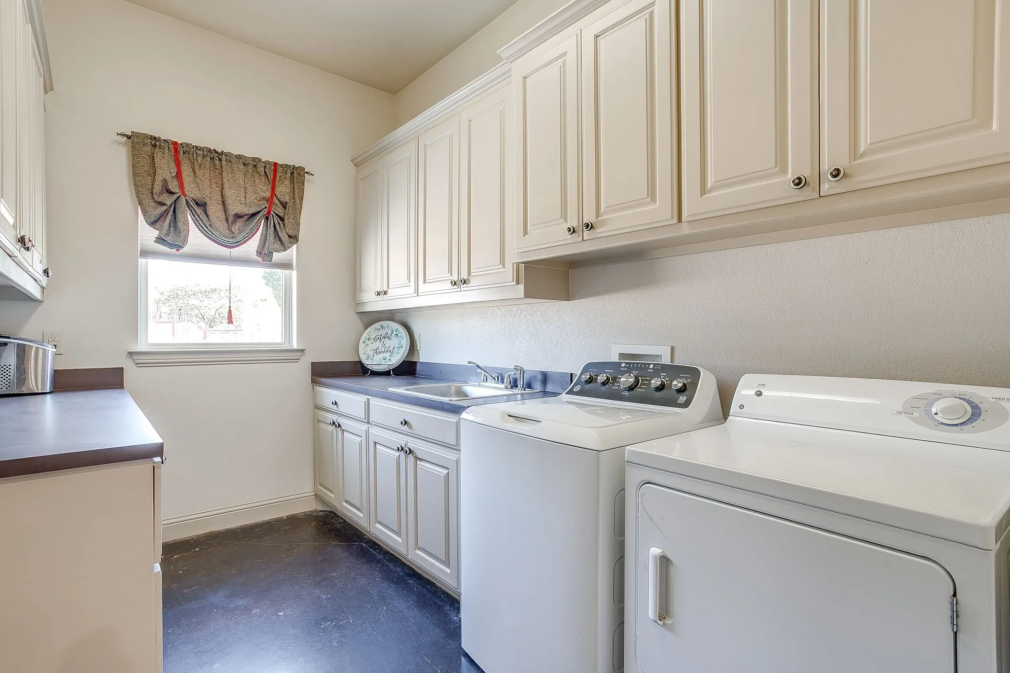 White shaker-style cabinetry, dark countertops, built-in sink, and a single window