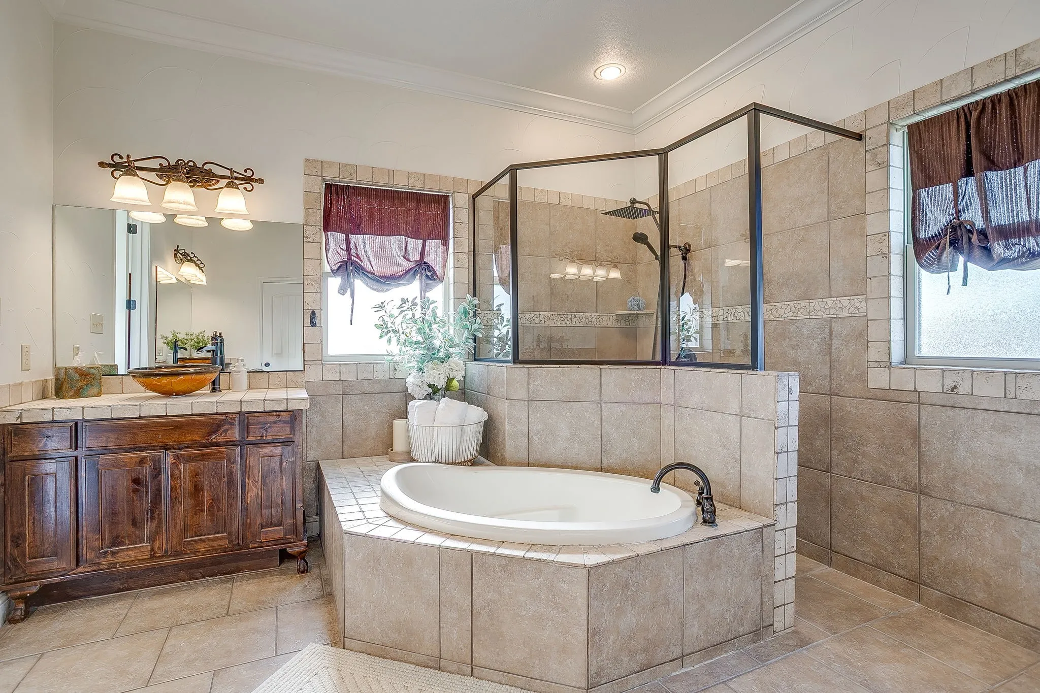Built-in corner bathtub, tiled shower enclosure with glass panels, wood-finish vanity with vessel sink, and overhead vanity lighting