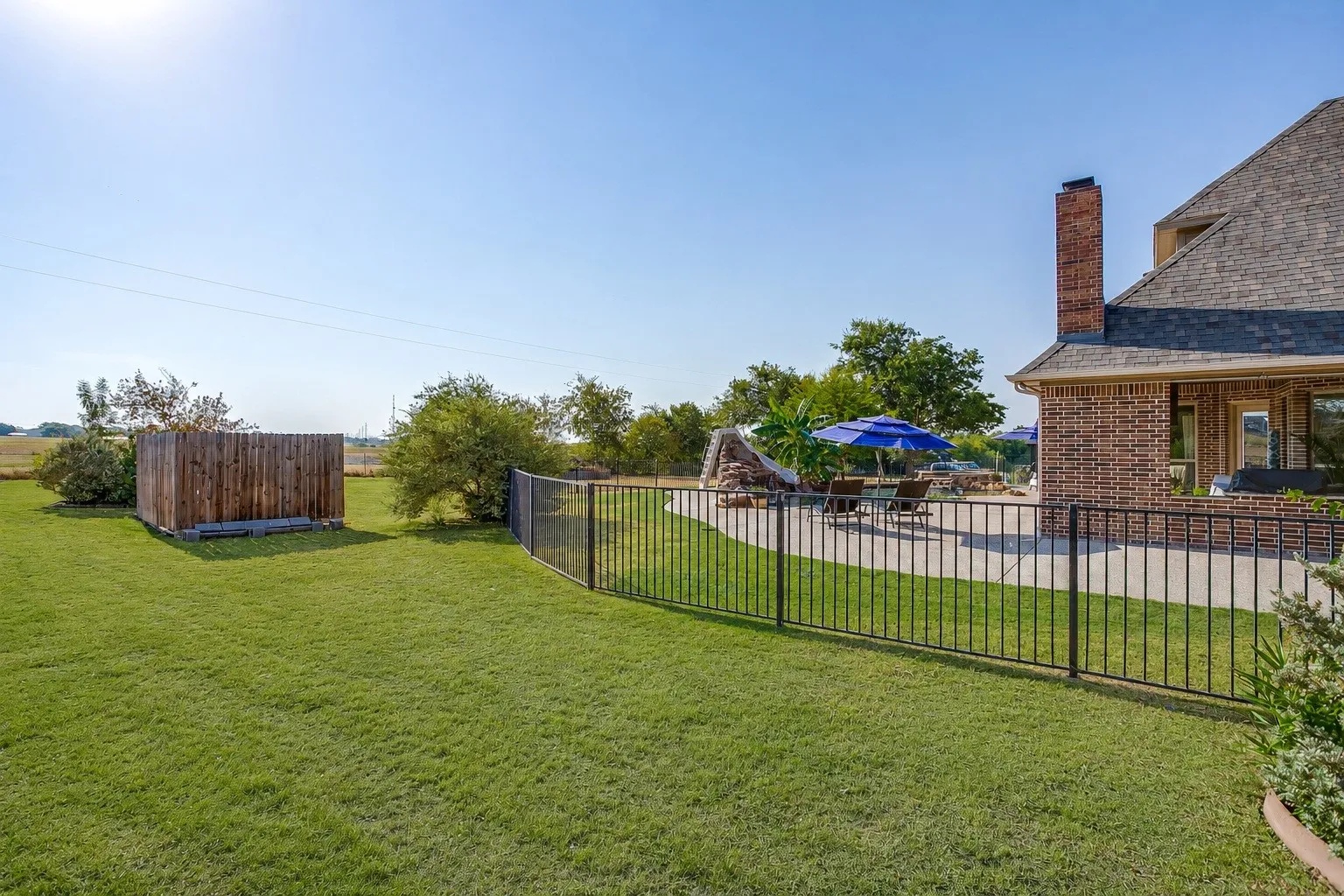 Expansive grass lawn with a wood privacy fence, black metal fencing, and an outdoor patio area