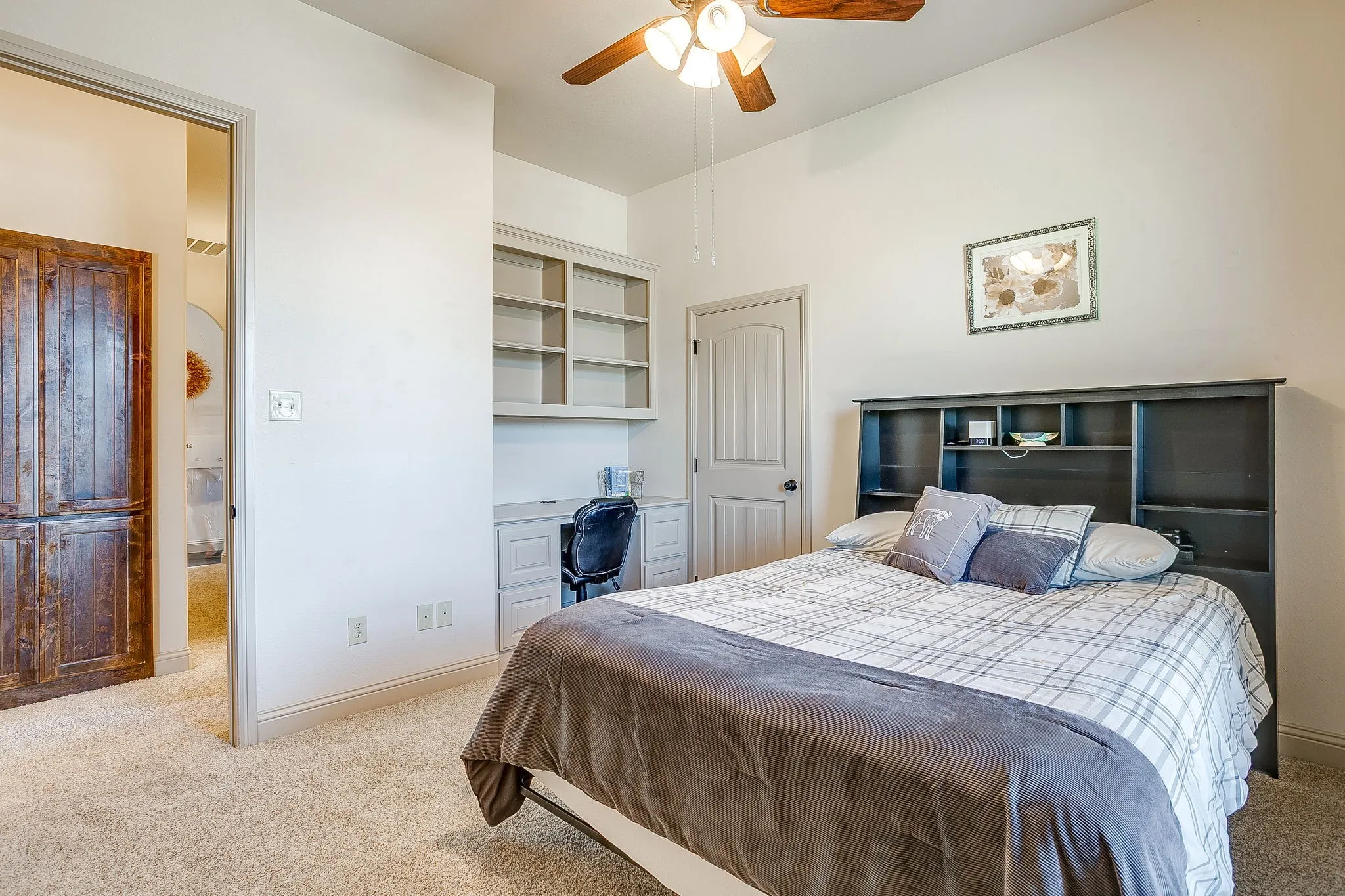 Bedroom 3 with vaulted ceiling with ceiling fan, built-in desk with shelving, light-colored carpet flooring, white paneled door