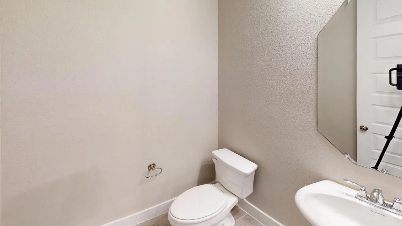 Pedestal sink with chrome fixtures, white toilet, and a frameless wall mirror