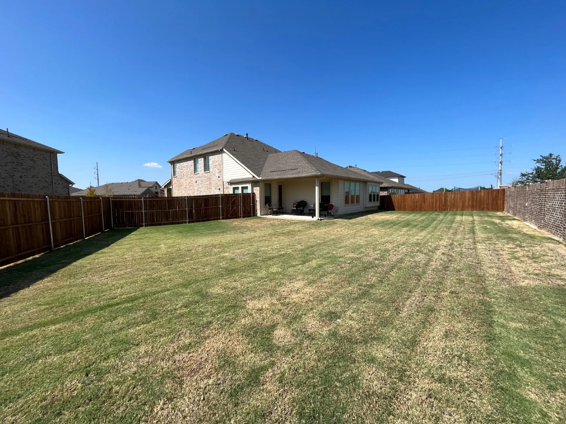 Expansive backyard with a covered patio, wood fencing, and a brick exterior