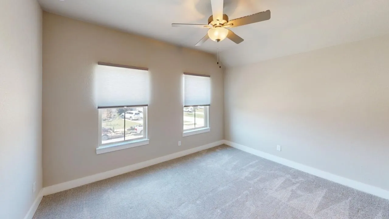 Neutral tone walls, vaulted ceiling, two windows with blinds, ceiling fan with integrated lighting, and carpeted flooring