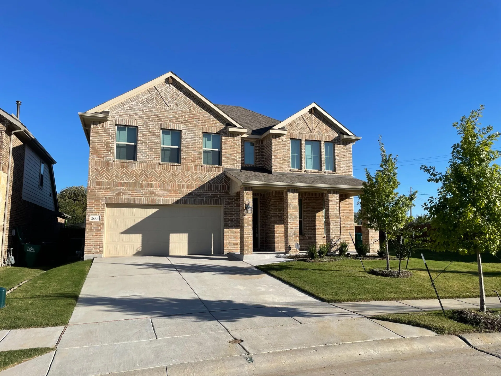 Brick exterior with decorative detailing, covered entry, attached garage, concrete driveway, and manicured lawn