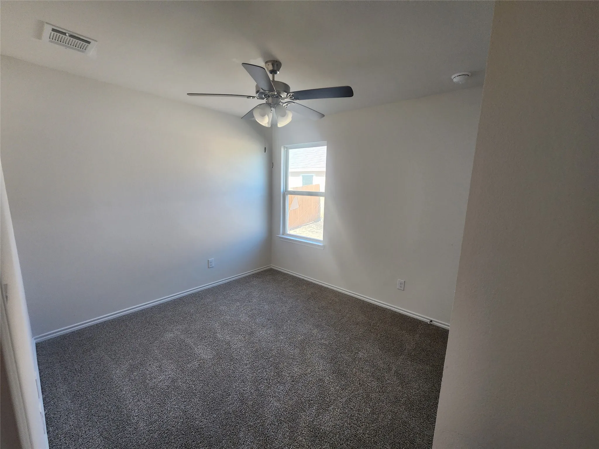 Bright interior space featuring a window, ceiling fan, and grey carpet flooring