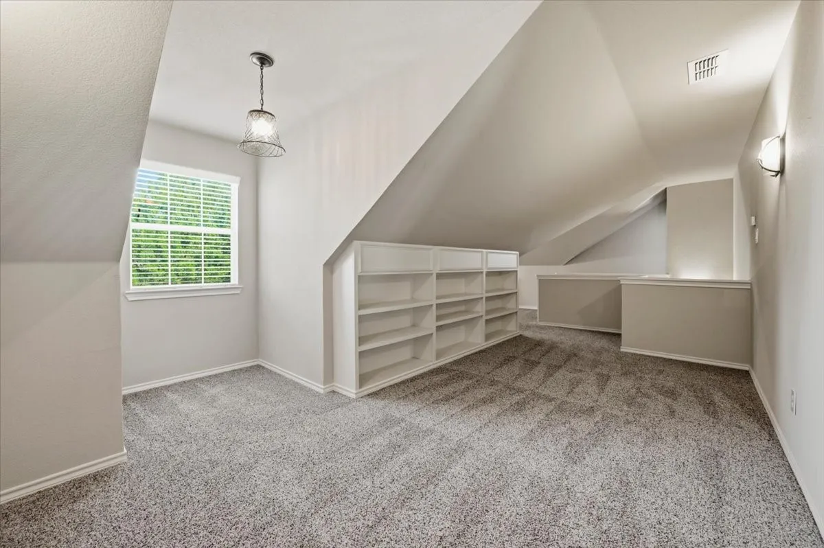 Spacious attic room with vaulted ceiling and center skylight, neutral wall finishes, and plush carpeting throughout