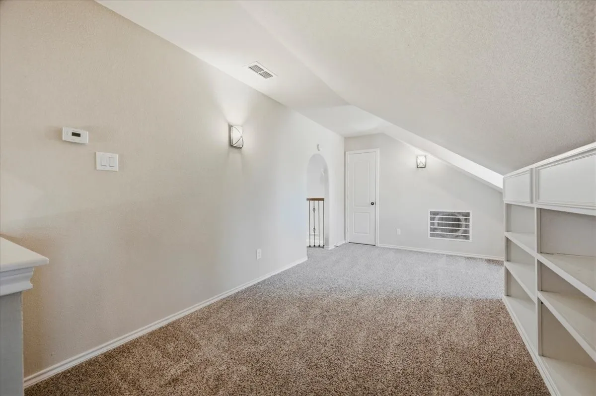 Bright attic bedroom featuring cathedral ceiling with peaked gable design, large fixed window with green trim, ceiling fan with integrated lighting, and neutral carpet flooring throughout