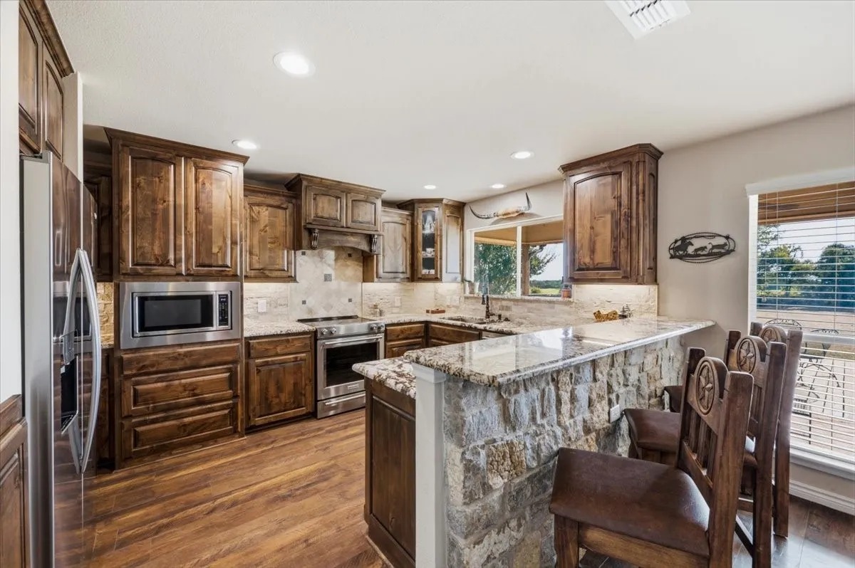 Kitchen featuring wood-finish flooring, stone-clad breakfast bar, stainless steel appliances, and wood cabinetry with undermount lighting