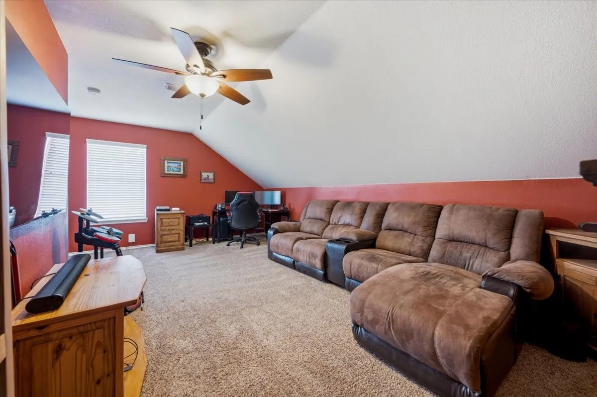 Carpeted loft area featuring a vaulted ceiling, built-in shelving, and an arched entryway with wrought iron railing