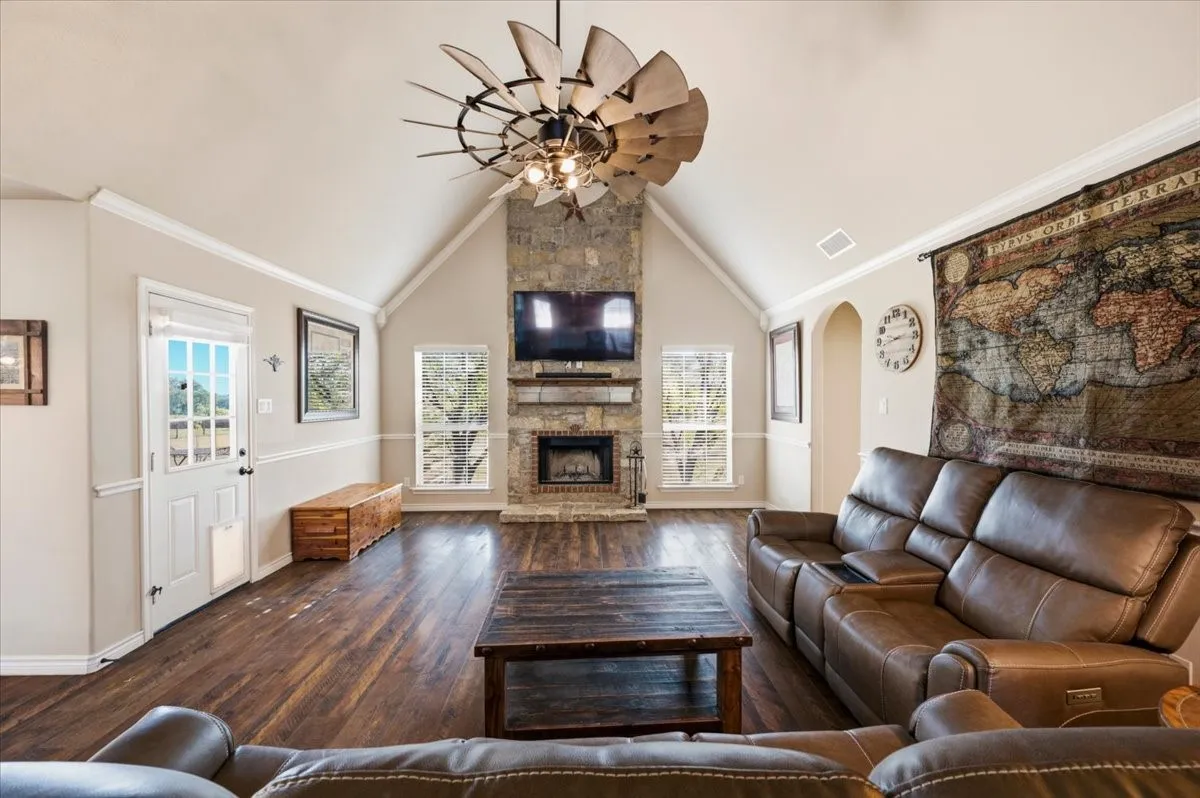 Vaulted ceiling with decorative fan, stone-clad fireplace, wood-finish flooring, and white trim molding
