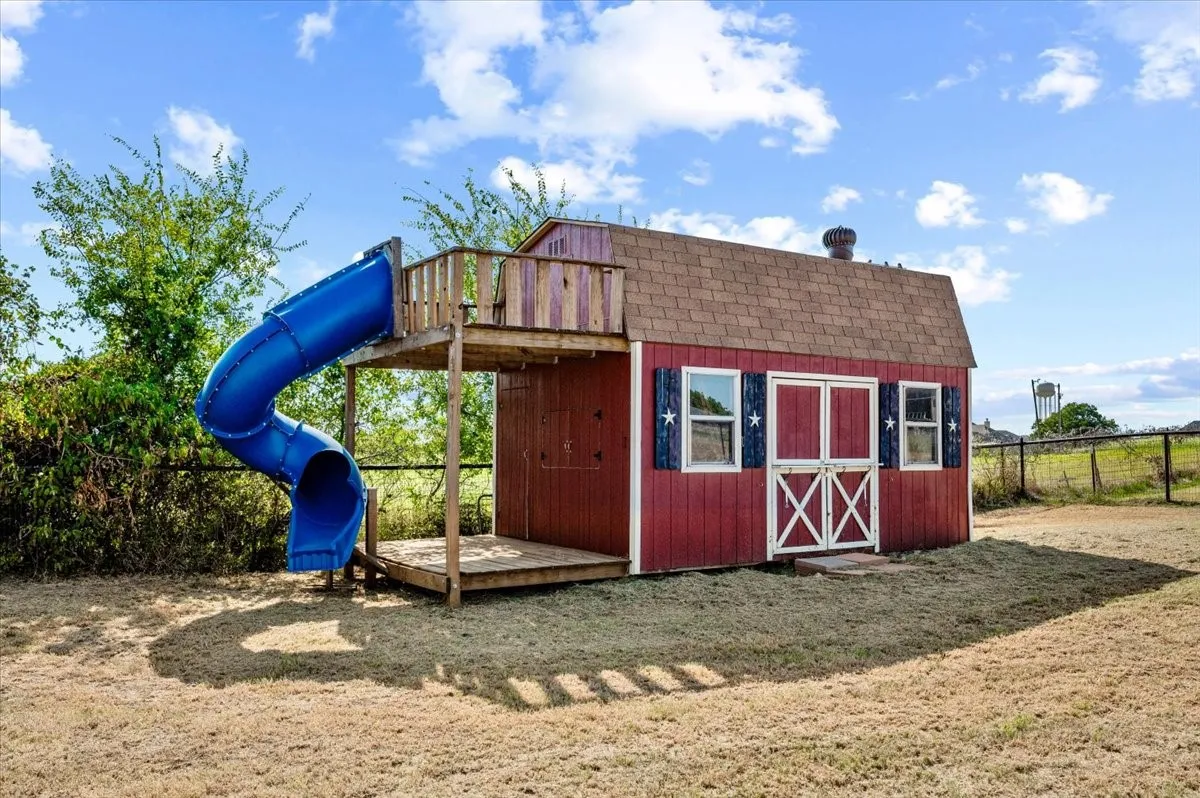 Two-story shed with a shingled roof, a wooden balcony, and an attached blue spiral slide