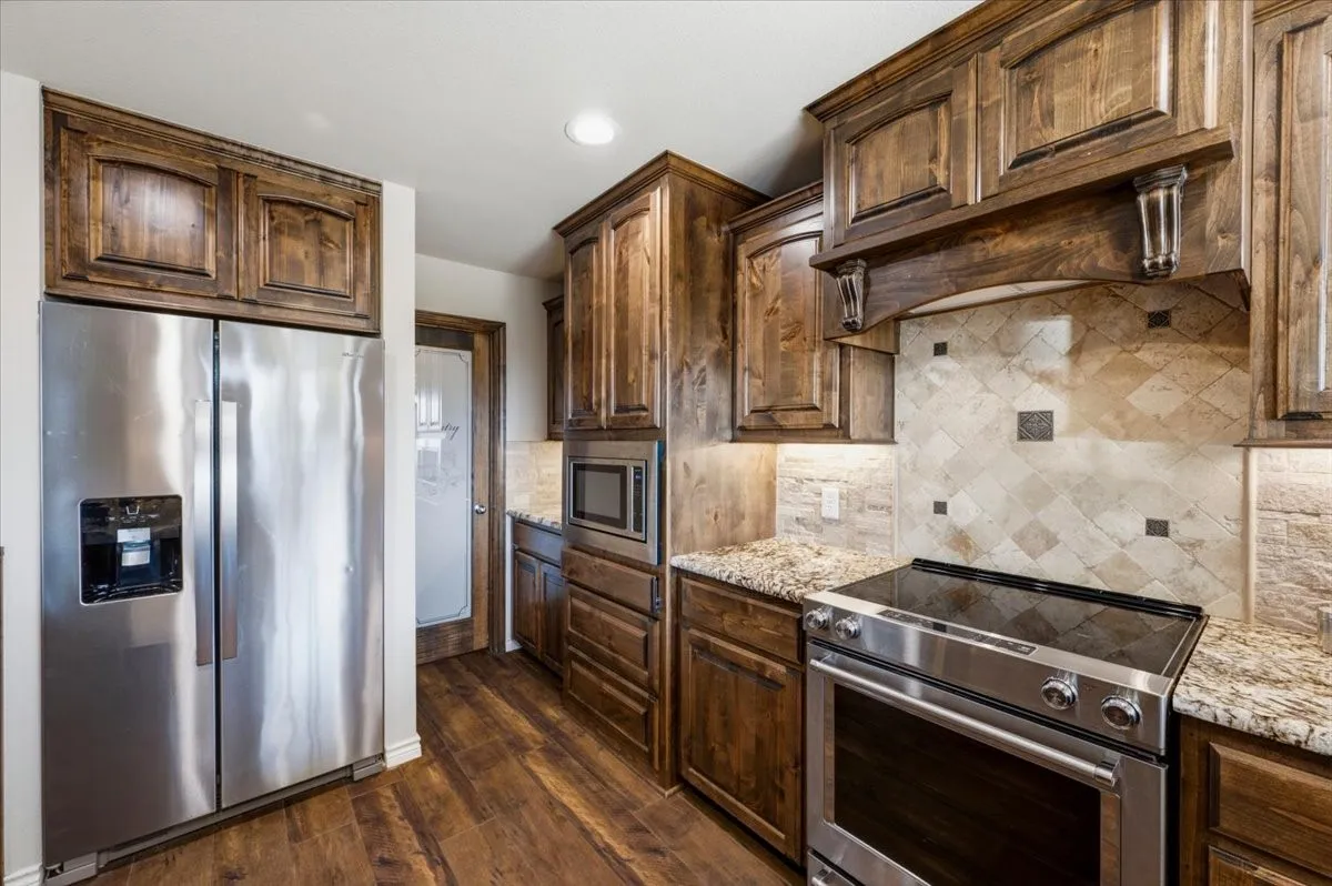 Wood-finish flooring, stainless steel appliances, granite countertops, wood cabinetry, and a decorative tile backsplash