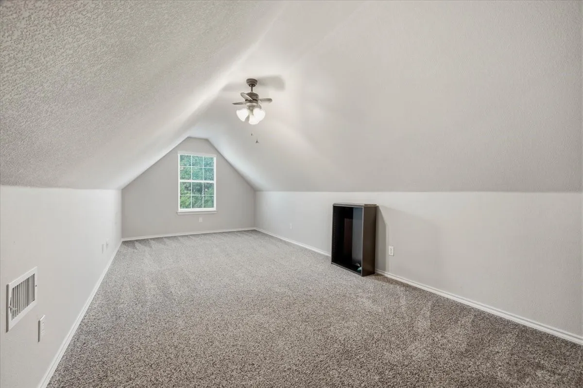 Spacious bonus room with vaulted ceilings, ceiling fan with integrated lighting, and plush wall-to-wall carpeting