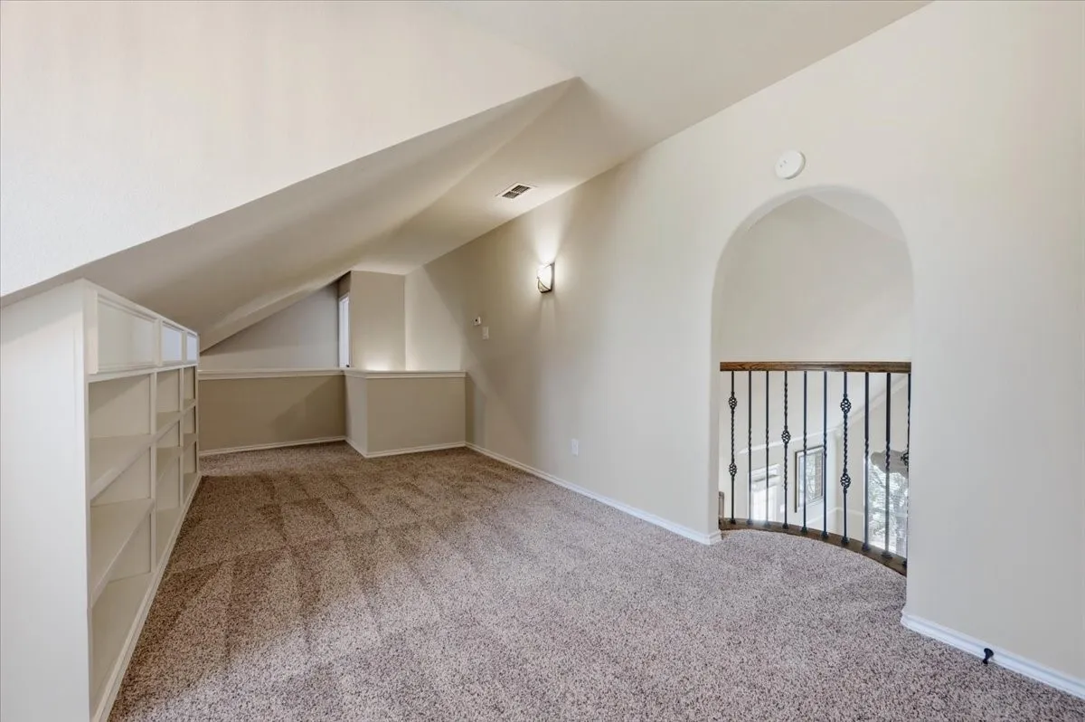 Expansive attic space with vaulted ceilings, abundant natural light from a dormer window, built-in shelving and storage cabinetry, carpeted flooring, and a pendant light fixture