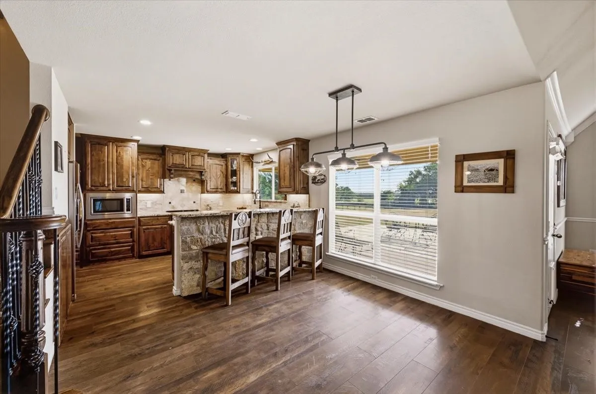 Open-concept kitchen and dining area featuring rich wood cabinetry, stainless steel appliances, wood-finish flooring throughout, and expansive windows providing natural light and outdoor vistas