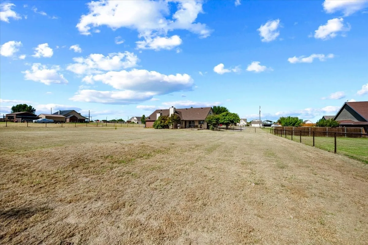 Expansive outdoor space featuring a brown fence and a distant residential structure