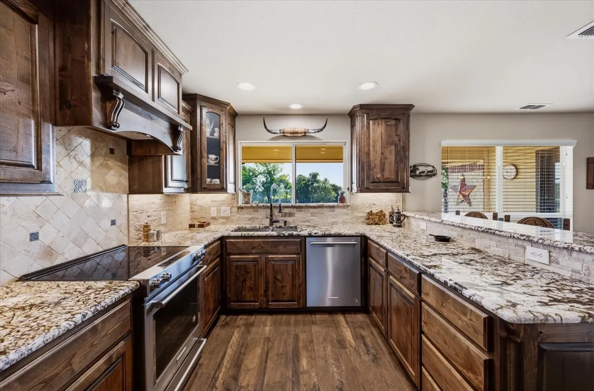 Kitchen featuring wood-finish flooring, granite countertops, tile backsplash, wood cabinetry, and stainless steel appliances