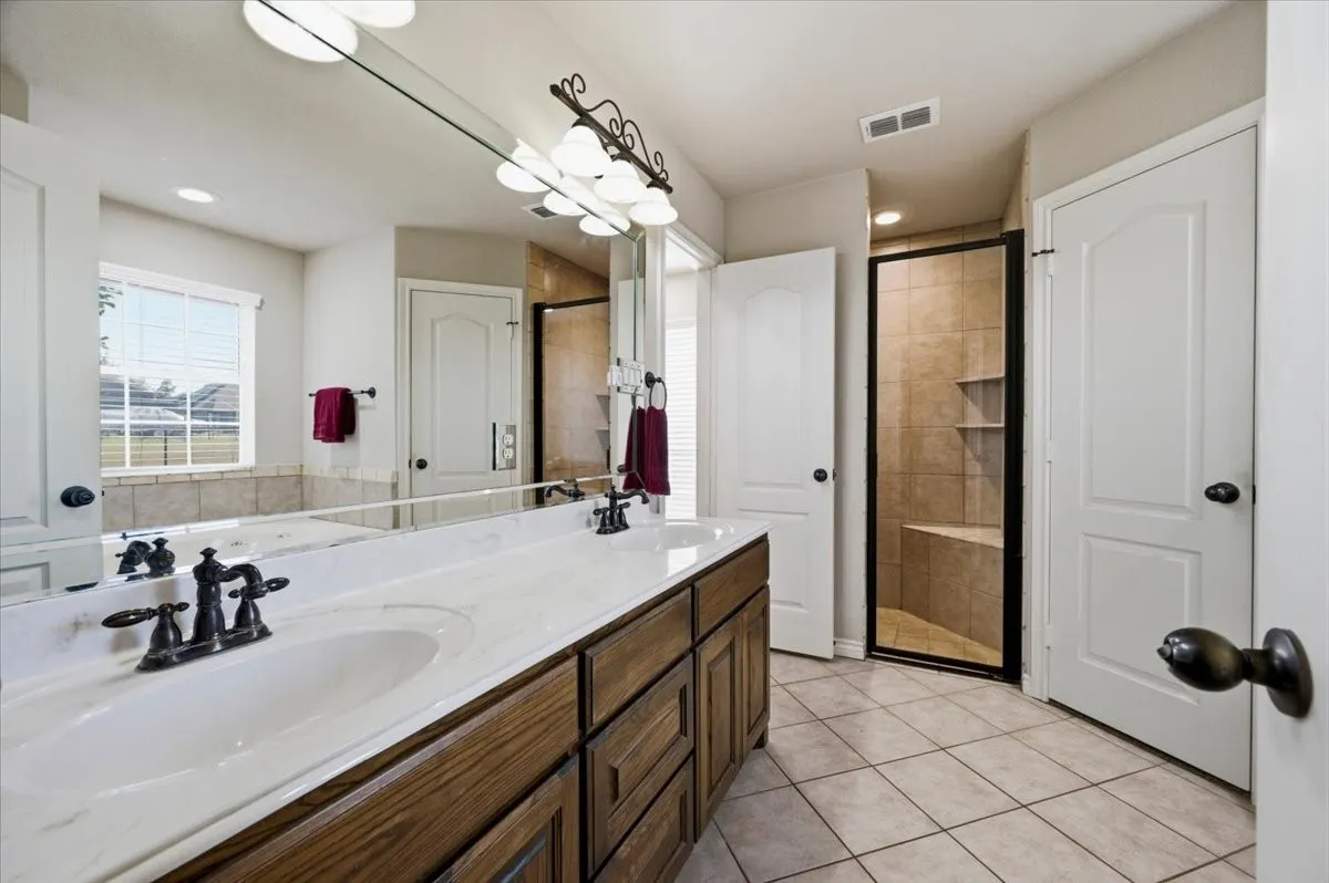 Spa-inspired master bathroom featuring dual vanities with wood-finish cabinetry, white quartz countertops, and oil-rubbed bronze faucetry