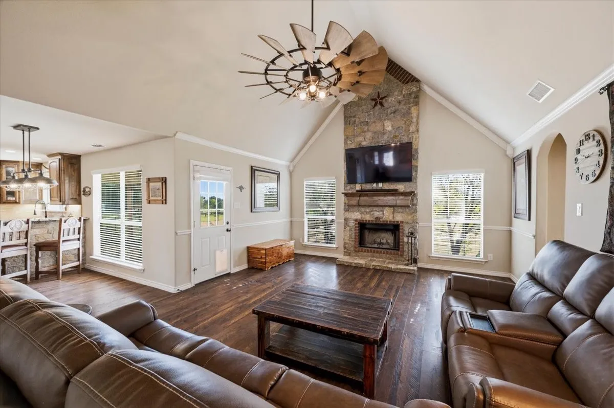 Vaulted ceiling, stone fireplace with mantel, wood-finish flooring, recessed lighting, and a unique ceiling fan