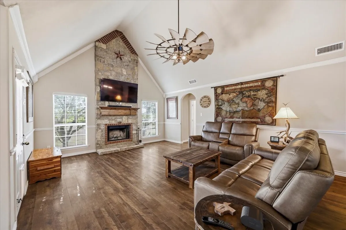 Vaulted ceilings, a stone-clad fireplace with a wood mantel, wood-finish flooring, and white trim molding throughout
