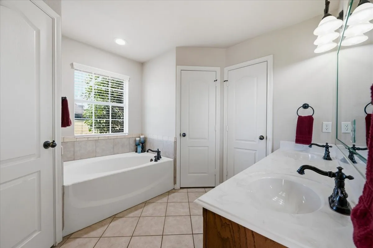 Spacious primary bathroom featuring dual vanities with white quartz countertops, matte black faucetry, and an alcove soaking tub positioned beneath a large window