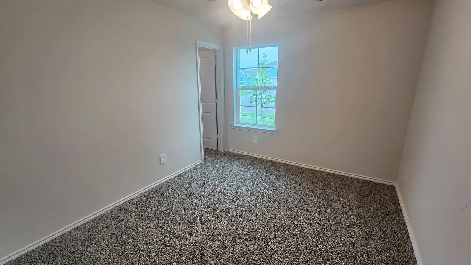 Neutral tone wall paint, textured carpeting, bright window, ceiling fan with light fixture, and white trim