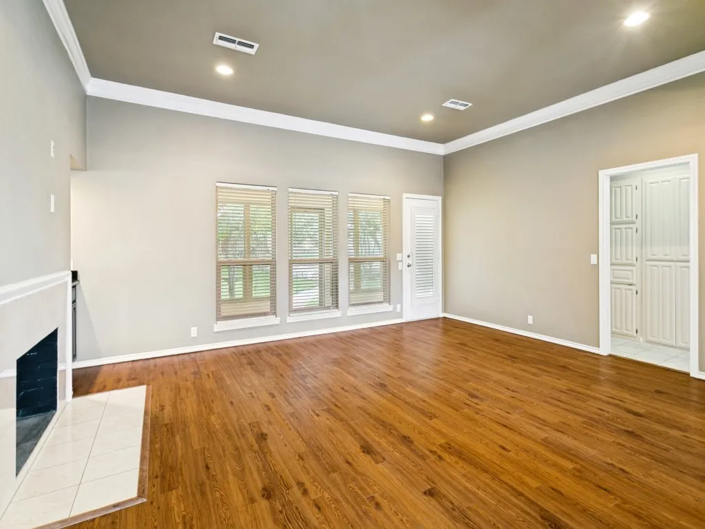 Vaulted ceiling with recessed lighting, wood-finish flooring, fireplace with tiled hearth, multiple windows, and a built-in storage cabinet