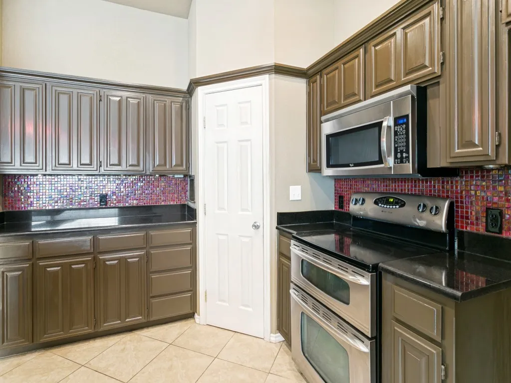 Kitchen featuring brown cabinetry, dark countertops, a vibrant mosaic tile backsplash, and stainless steel appliances including a double oven range and microwave