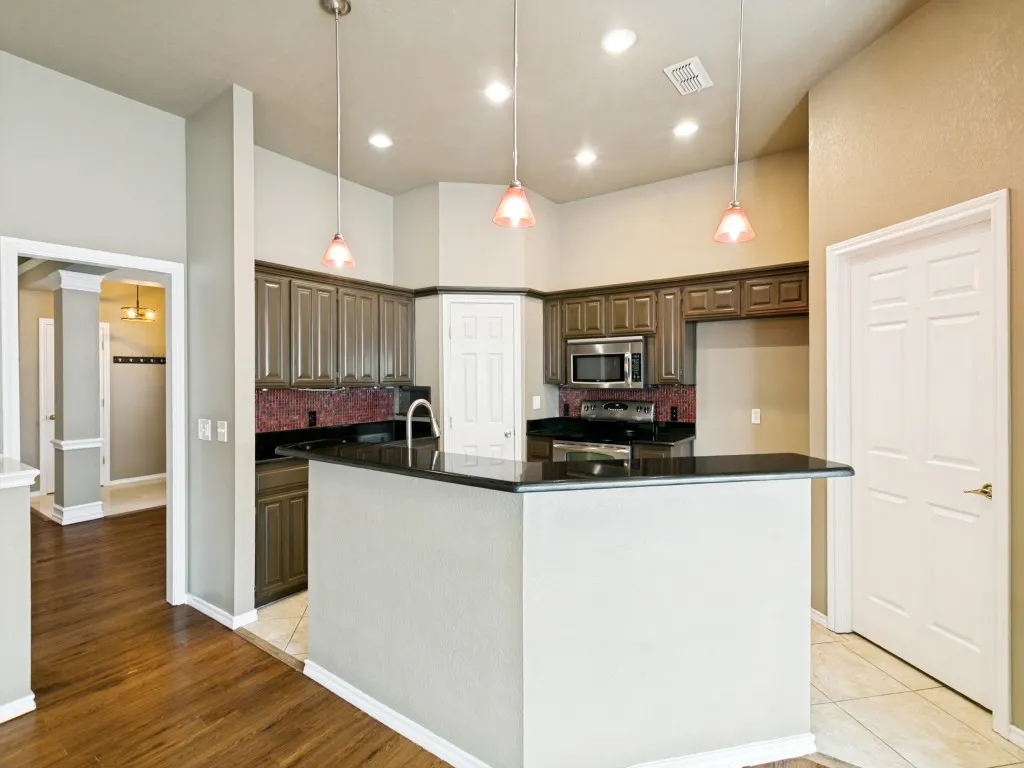 Kitchen featuring dark wood cabinetry, black countertops, stainless steel microwave, recessed lighting, and pendant lighting