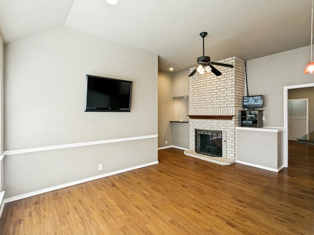 Vaulted ceiling with recessed lighting, wood-finish flooring, white brick fireplace with hearth, built-in shelving, and a ceiling fan with light kit