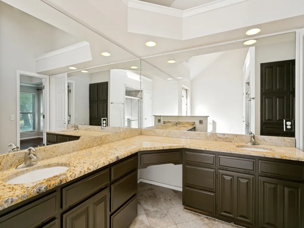 Dual undermount sinks with chrome faucets, ample counter space with stone-finish countertops, custom dark cabinetry, and integrated ceiling lighting
