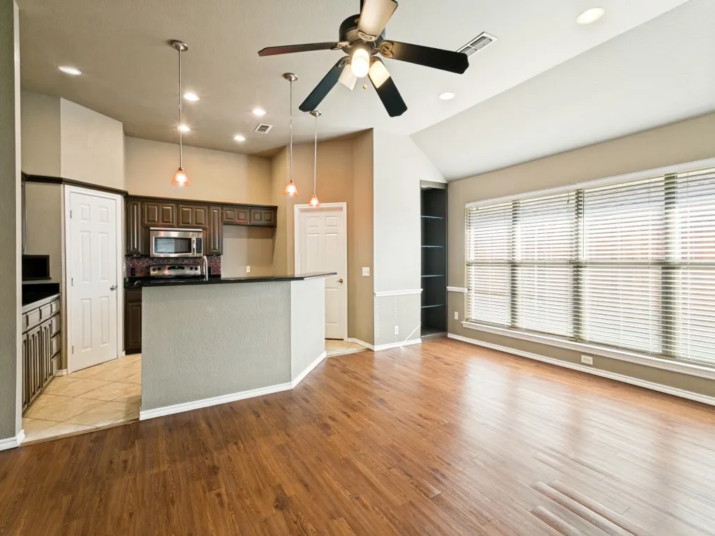 Wood-finish flooring, vaulted ceiling, built-in shelving, dark wood cabinetry, and a kitchen island with pendant lighting