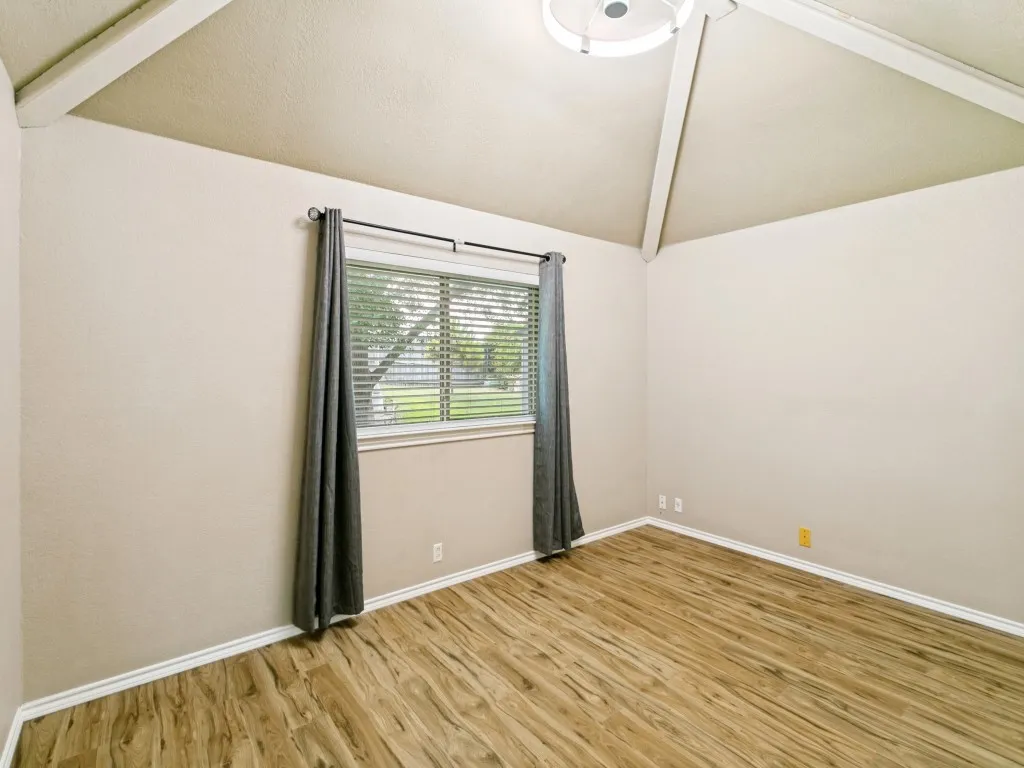Vaulted ceiling with exposed beams, wood-finish flooring, and a single window