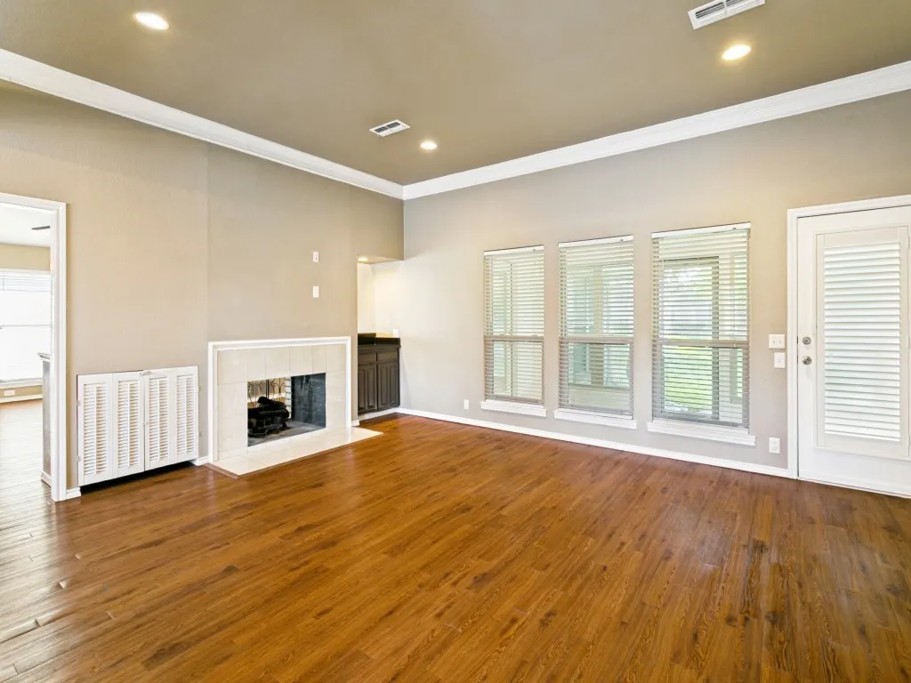 Wood-finish flooring throughout, featuring a fireplace with a light-toned surround, recessed lighting, and crown molding
