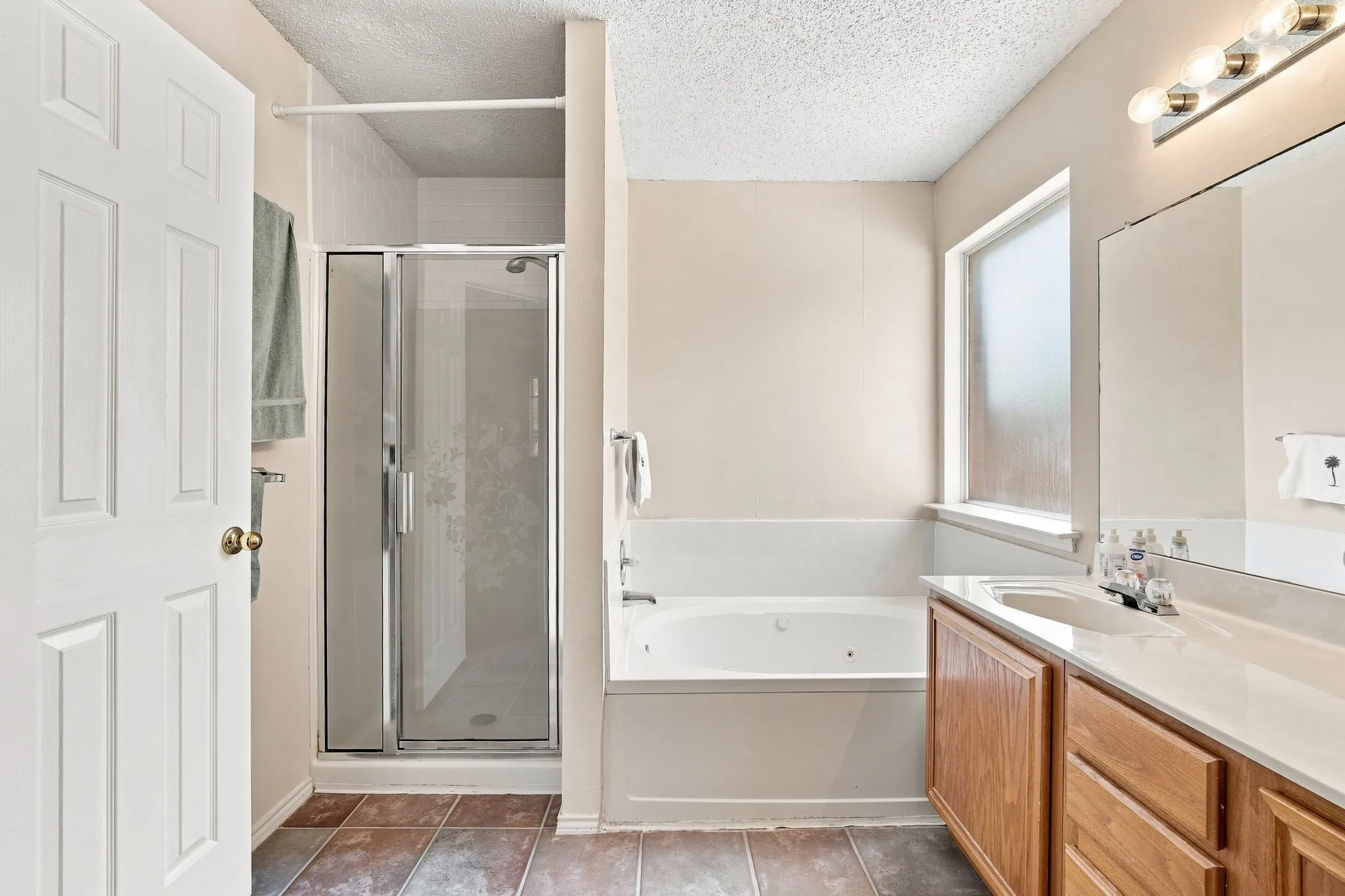 Shower with glass enclosure, built-in bathtub, wood-finish vanity with integrated sink, and frosted window
