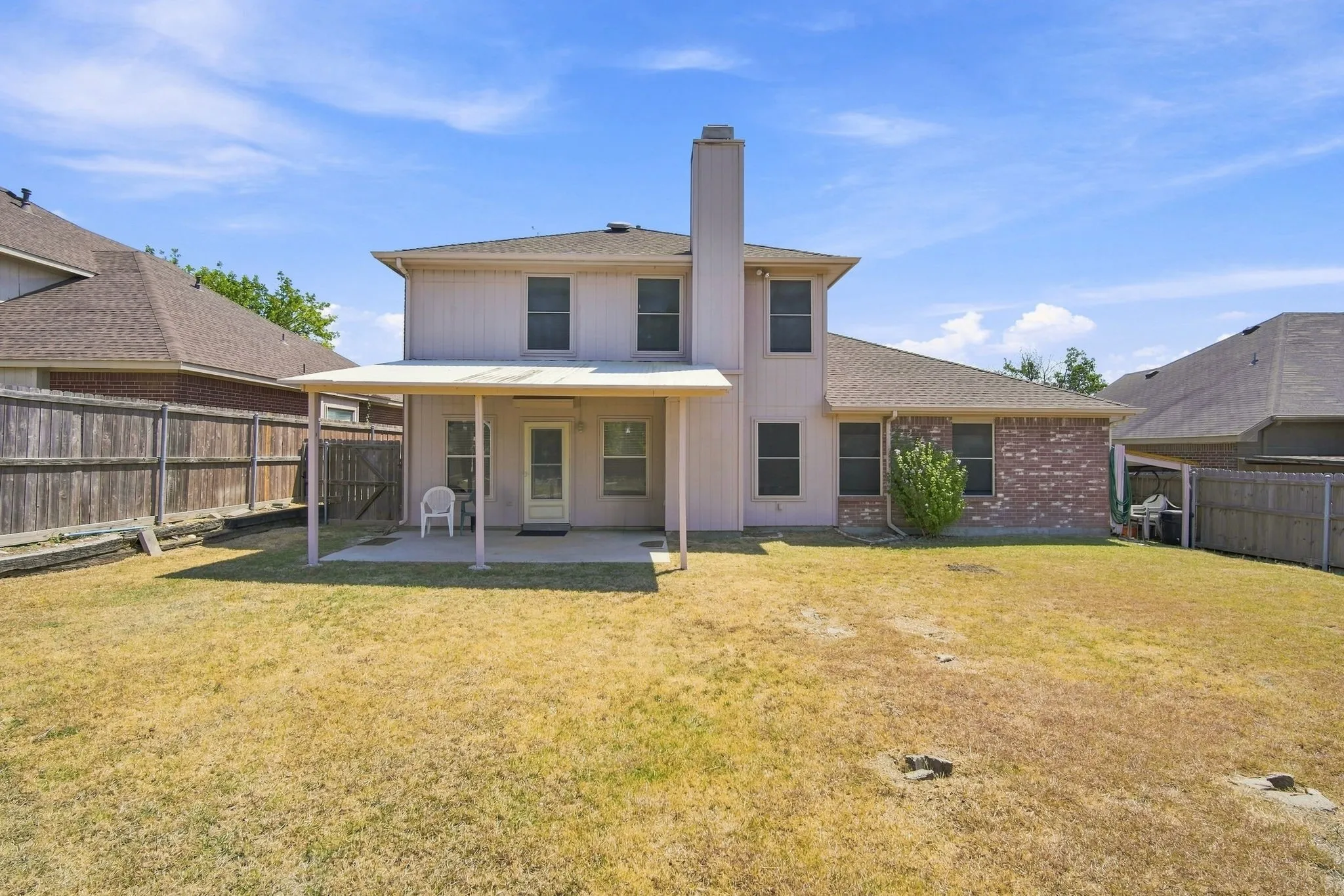 Private backyard with a covered patio, wood fencing, and a brick and siding exterior