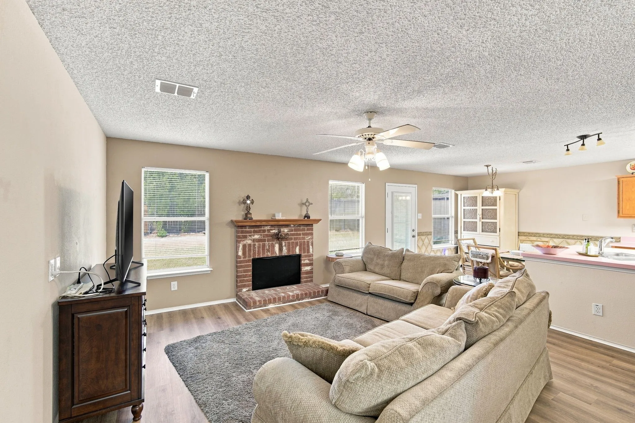 Brick fireplace with mantel, wood-finish flooring, ceiling fan, recessed lighting, and track lighting