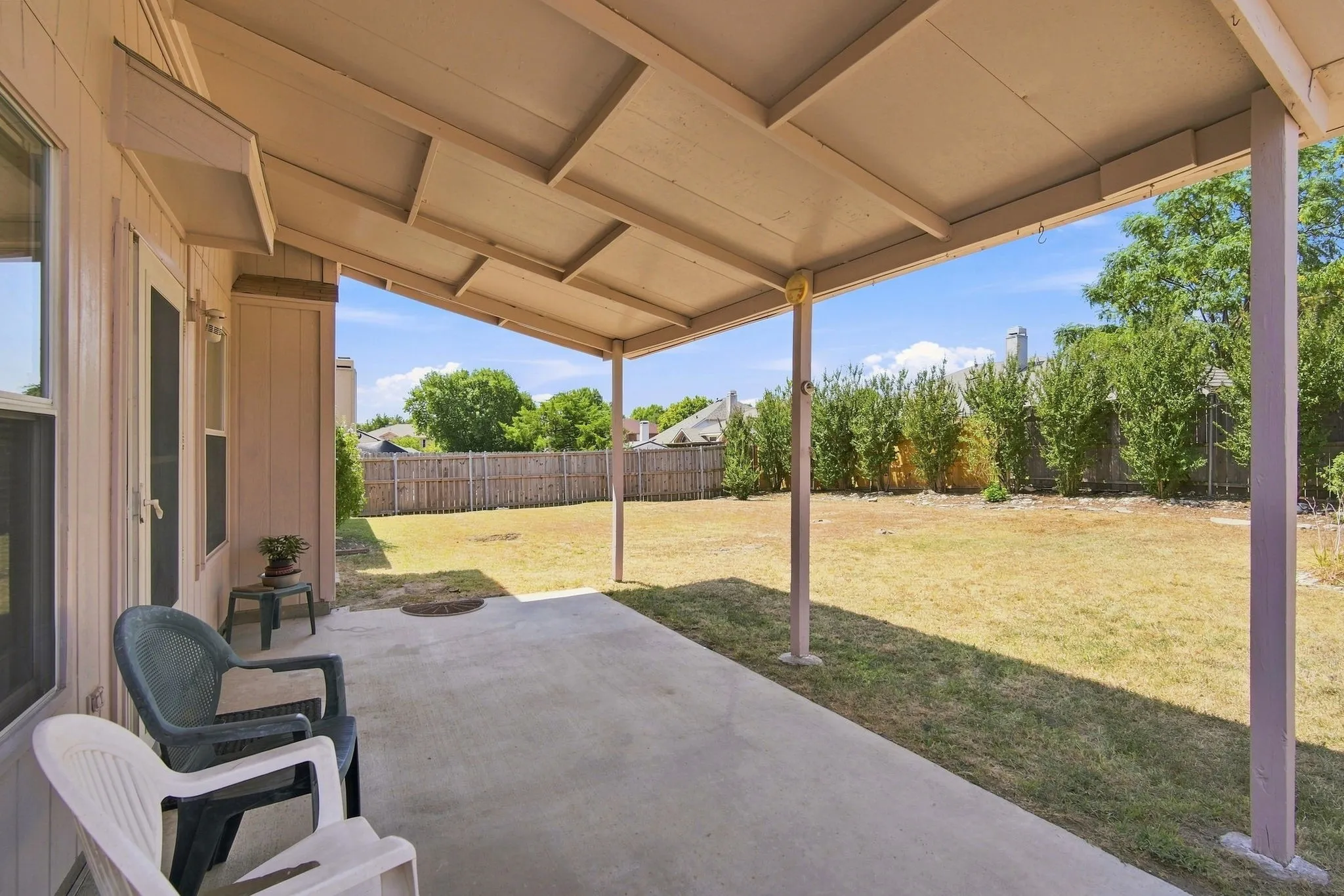 Expansive covered patio with concrete flooring, supported by multiple posts, opening to a large backyard with a privacy fence