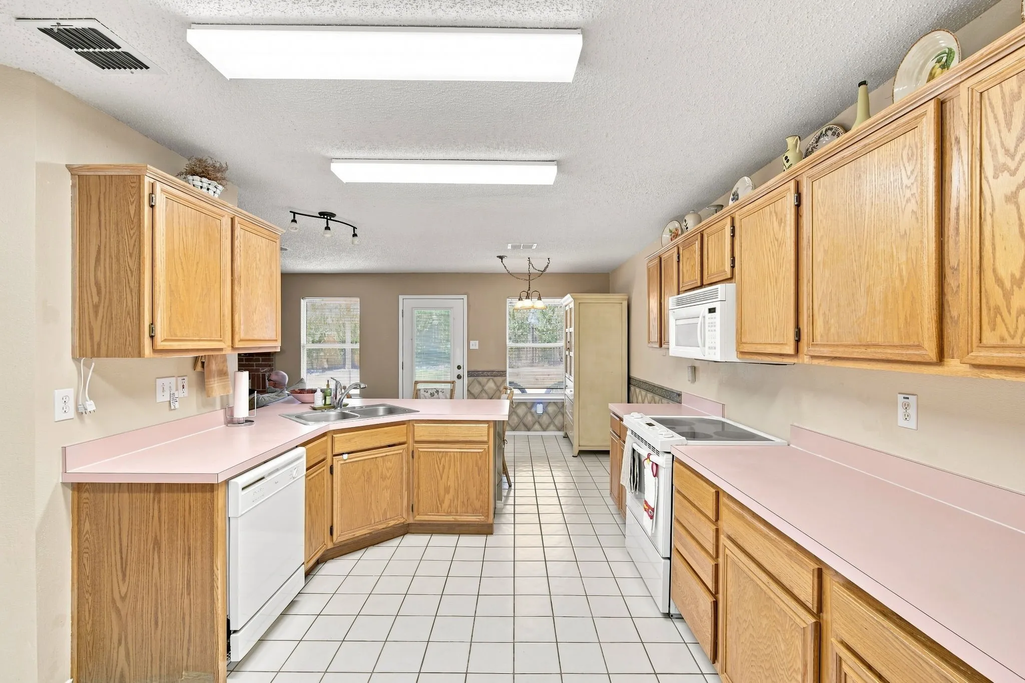 Expansive kitchen featuring wood-finish cabinetry, white tile flooring, and light-colored countertops