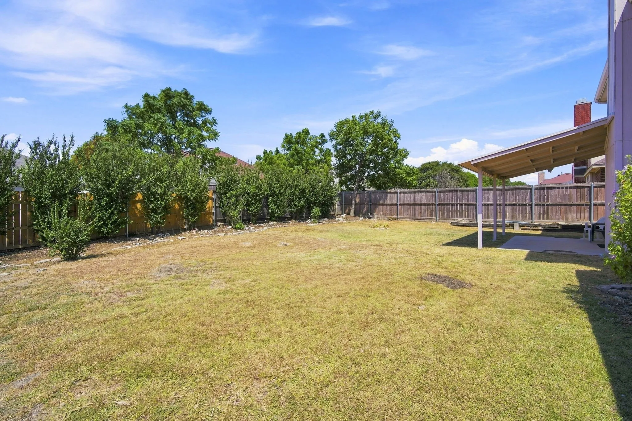 Spacious backyard featuring a covered patio, wood privacy fence, and mature perimeter landscaping