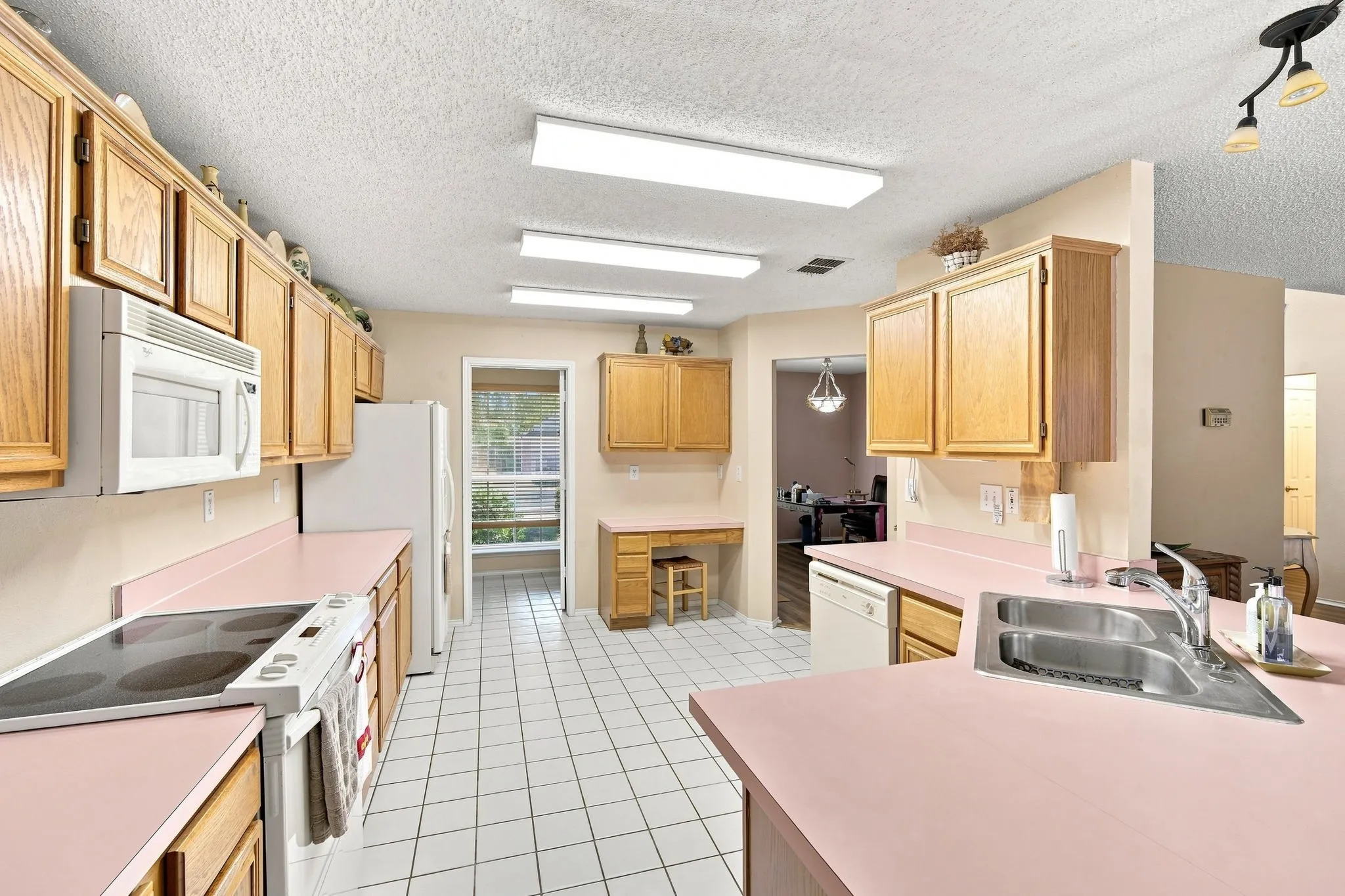 Kitchen featuring light wood cabinetry, pink countertops, white tile flooring, and a stainless steel double basin sink