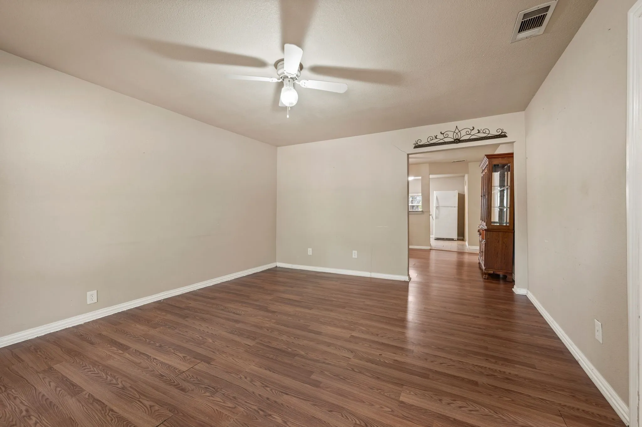 Wood-finish flooring throughout, neutral paint, ceiling fan light fixture, and arched doorway with decorative ironwork