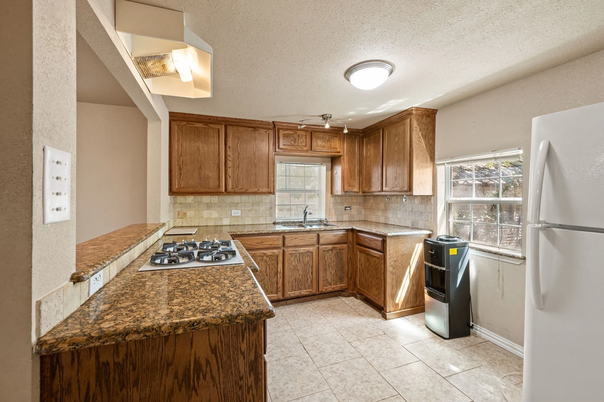 Kitchen featuring wood cabinetry, a built-in gas cooktop, tile flooring, and a tile backsplash