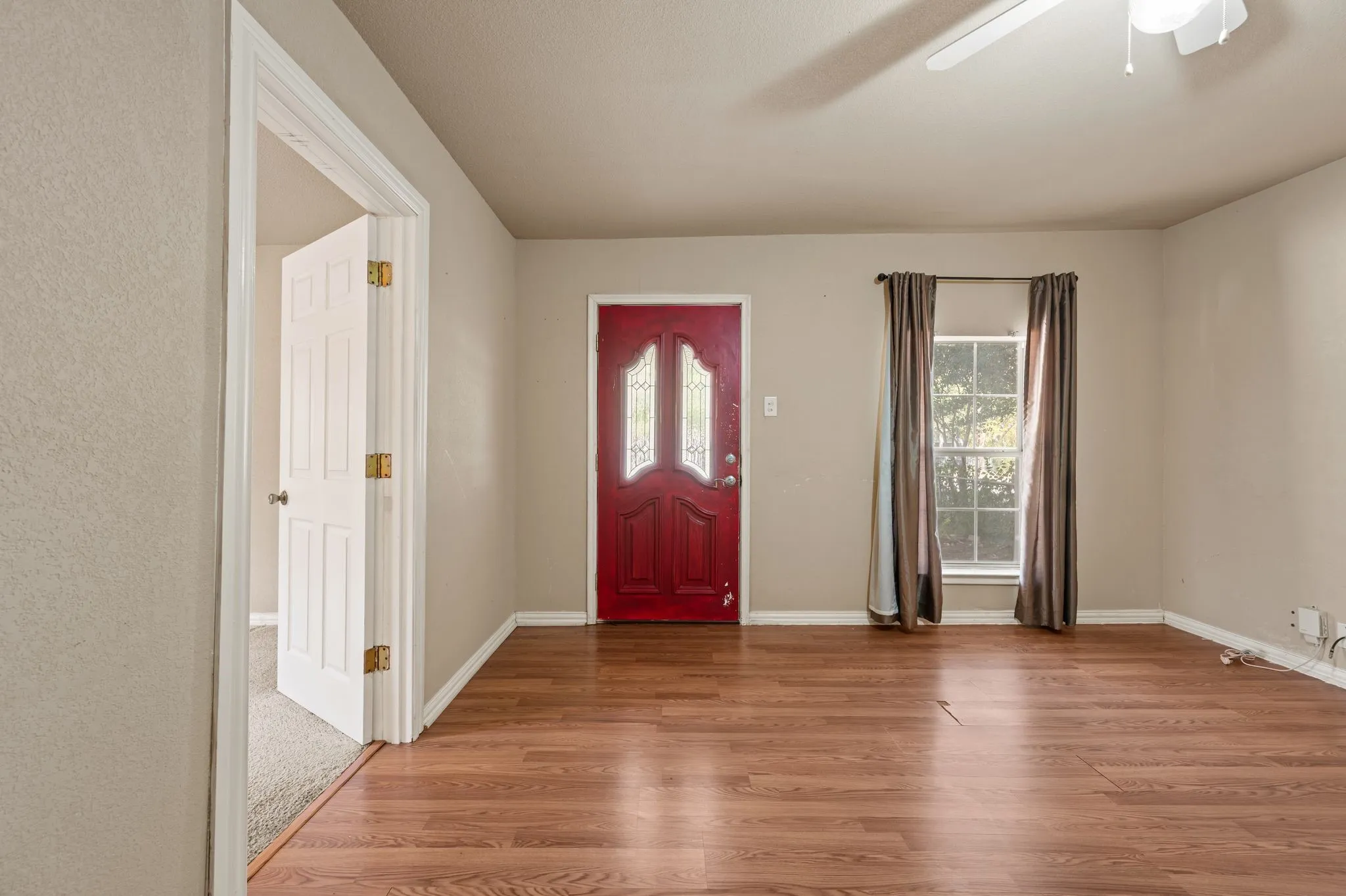 Wood-finish flooring, red entry door with decorative glass, window with natural light, ceiling fan with light fixture, and neutral wall tones