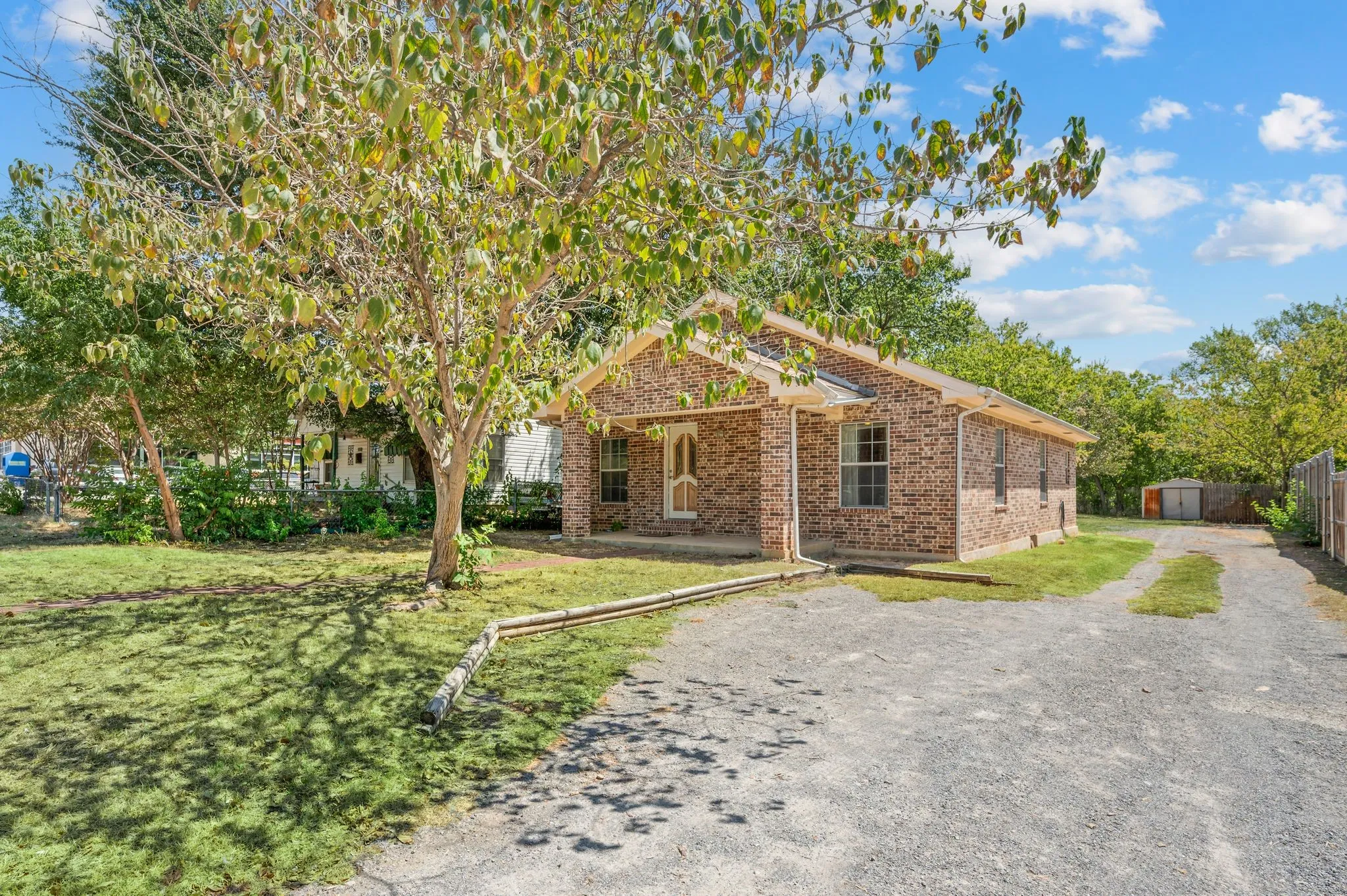 Brick facade residence with a covered front porch, gravel driveway, and a detached storage shed