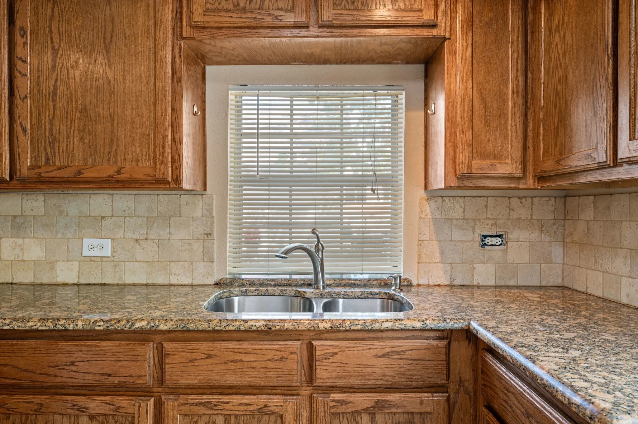 Wood cabinetry and stone-finish countertops frame a double basin stainless steel sink