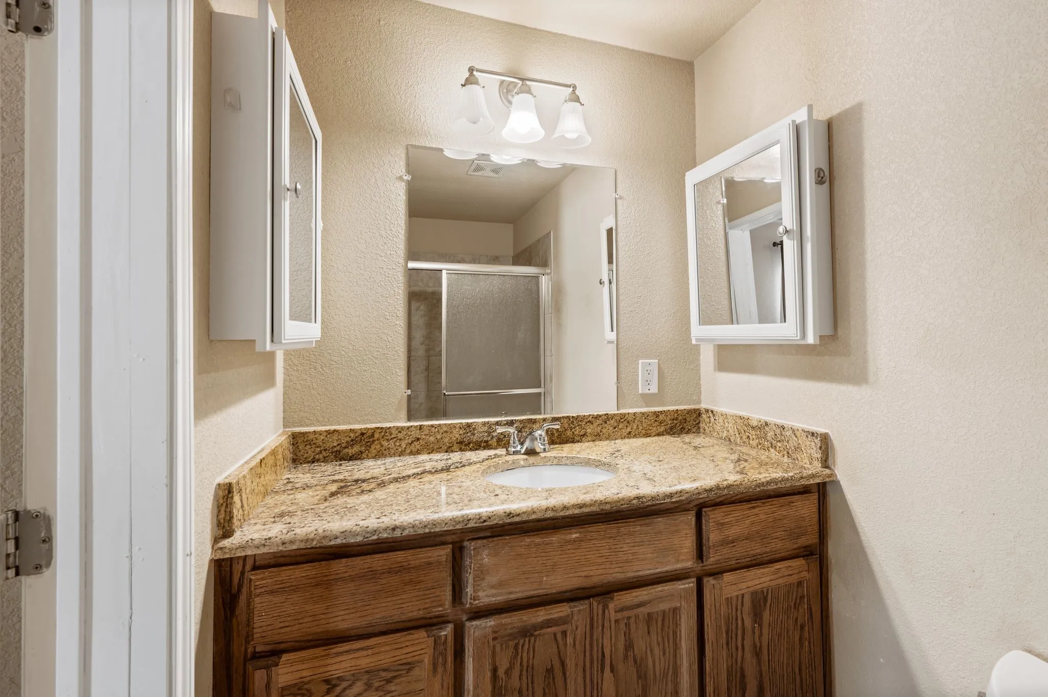 Vanity with a built-in sink, stone countertop, wood-finish cabinetry, and wall-mounted medicine cabinets
