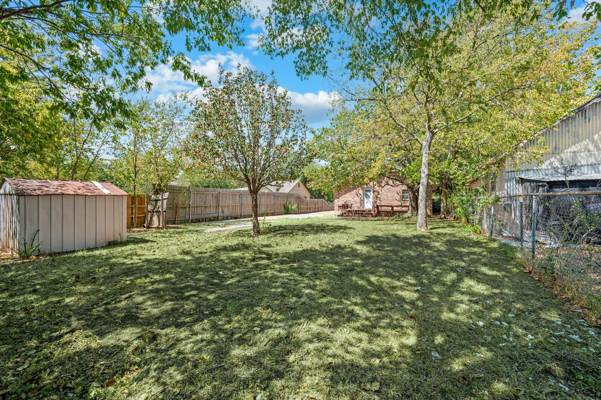 Expansive backyard featuring a manicured lawn, established trees, a storage shed, and a privacy fence