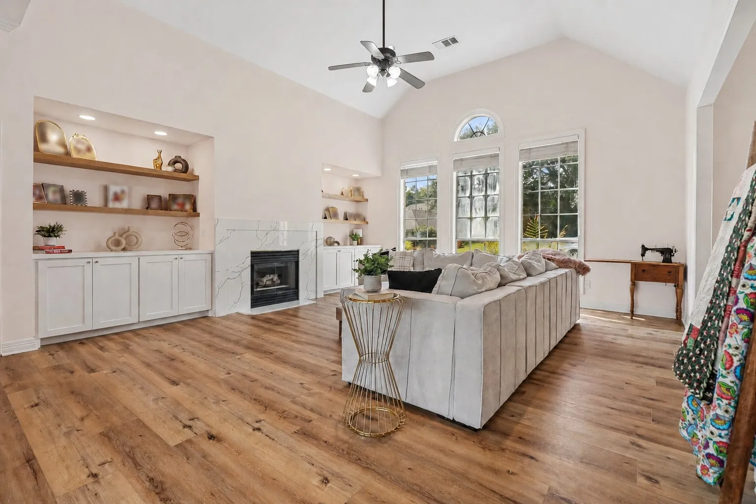 Vaulted ceiling with a ceiling fan, recessed lighting, wood-finish flooring, built-in shelving, and a fireplace with a stone surround